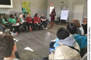 Woman talking in a room to a circle of people. Flip chart at back of room