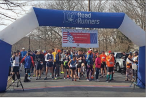 Runners gathered at the start of the race. You see them through a large arch colored blue and white