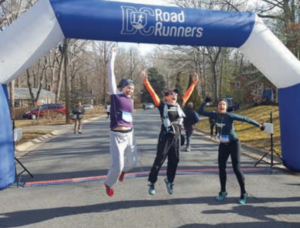 Three people under the large blue and white arch jumping up with arms in the air and mouths open, celebrating their completion of the race 